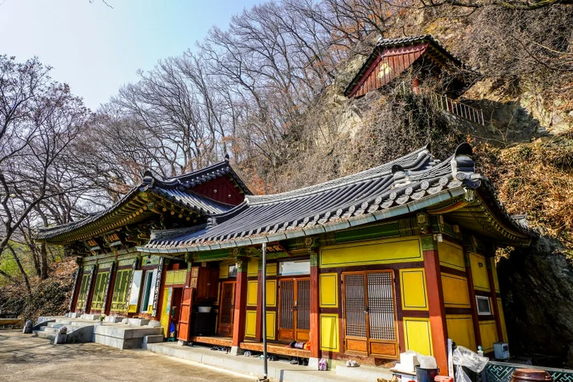 A wide exterior view of traditional Korean temple buildings with grey tiled roofs and yellow walls, nestled on a hillside surrounded by bare trees. - 全州(チョンジュ)西古寺(ソゴサ)で心癒すテンプルステイ体験：静寂の中で見つける本当の自分