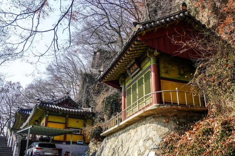 Multiple traditional Korean temple buildings with red and yellow accents, built into a rocky hillside with sparse winter vegetation. - 全州(チョンジュ)西古寺(ソゴサ)で心癒すテンプルステイ体験：静寂の中で見つける本当の自分
