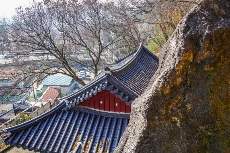 An overhead view of traditional Korean temple rooftops with dark tiles and red eaves, seen from a higher vantage point with bare tree branches. - 全州(チョンジュ)西古寺(ソゴサ)で心癒すテンプルステイ体験：静寂の中で見つける本当の自分