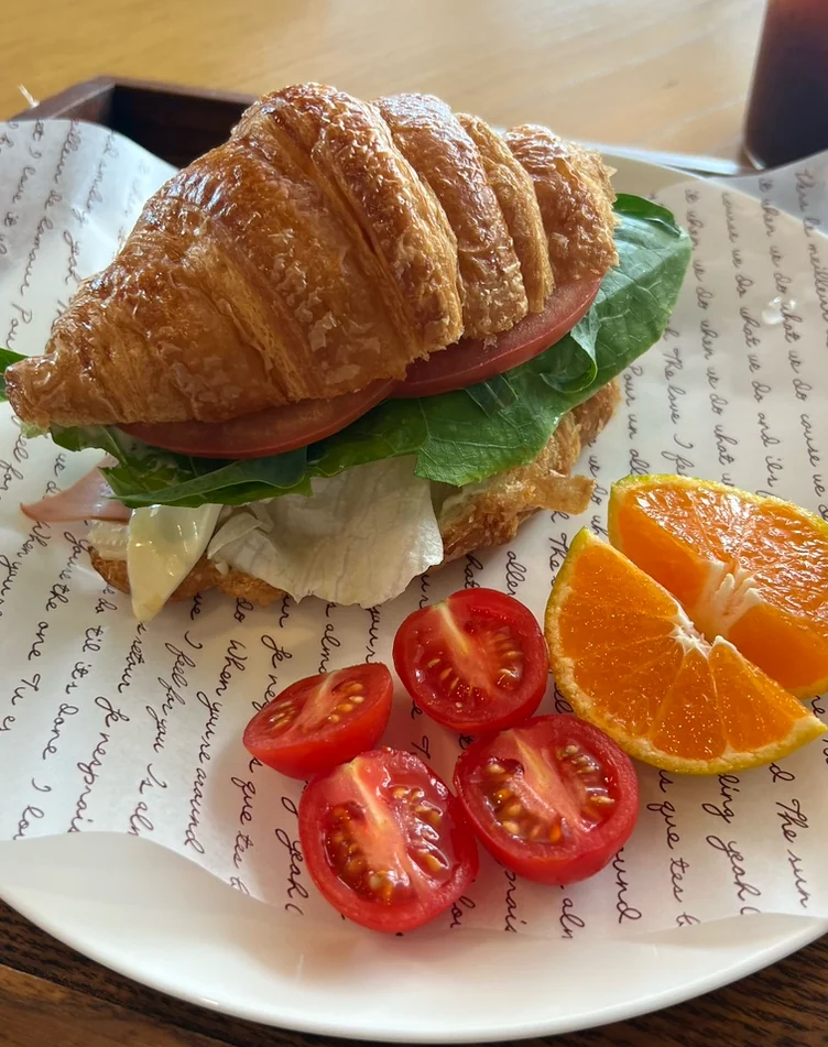 A croissant sandwich served with sliced tangerines and cherry tomatoes on a white plate - 済州島・涯月(エウォル)の静かな休息地。ミッカン倉庫(Mikkang Changgo)で過ごす、蜜柑の香りに包まれた休日
