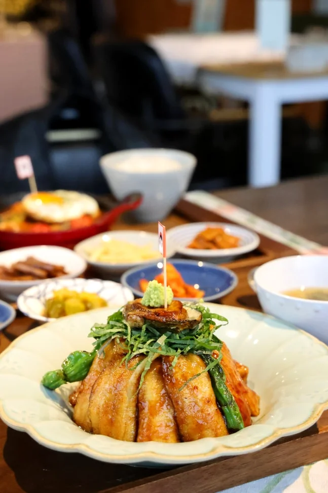 A bowl of rice topped with grilled meat and greens with small side dishes on a wooden tray - 済州島・涯月(エウォル)の静かな休息地。ミッカン倉庫(Mikkang Changgo)で過ごす、蜜柑の香りに包まれた休日