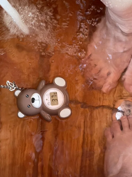 따뜻한 족욕물에 발을 담그고 있는 모습. 귀여운 곰돌이 온도계가 있어 아기자기한 감성을 더하며, 체험의 편안함을 보여줍니다. - ソウル薬令市韓医学博物館：五感で巡る、韓国伝統医療の魅力と癒し体験🌿