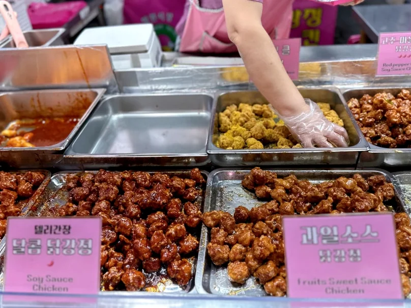 Trays of sweet & spicy dakgangjeong and soy sauce dakgangjeong at a stall, with a gloved hand serving. - Q's Dakgangjeong: A Culinary Gem in Seoul's Bustling Mangwon Market