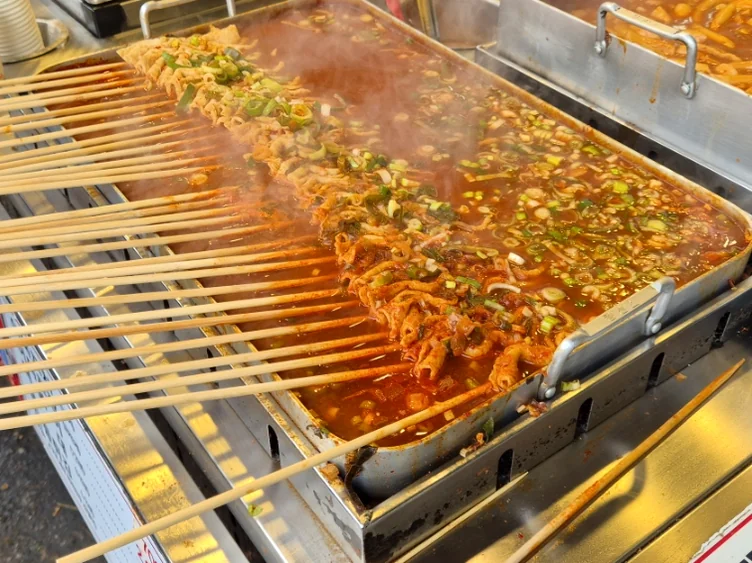 Multiple skewers cooking in a pan with sauce. - Q's Dakgangjeong: A Culinary Gem in Seoul's Bustling Mangwon Market