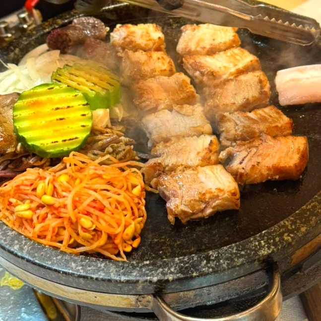 Various meats, zucchini, and bean sprouts grilling on a circular stone hot plate. - Exploring Hip-dang-dong's Dual Charm: From Shamanic Cocktails to Lee Young-ja's Favorite Meat Spot