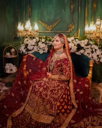 She seated in bridal finery, surrounded by lush floral arrangements.