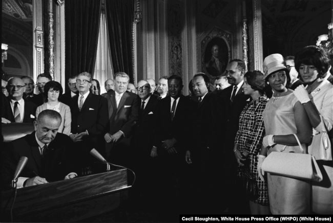 Until civil rights laws, many schools, businesses, and public buildings such as libraries and pools were segregated by race. Here, Johnson signs the Civil Rights Act of 1964. Martin Luther King, Jr. and other leaders look on. 在民权法案到来之前，很多学校、商业和公共建筑，比如图书馆和游泳池都因种族隔离。照片中，约翰逊正在签署《1964年民权法案》。马丁·路德·金和其他领导人在旁观看。