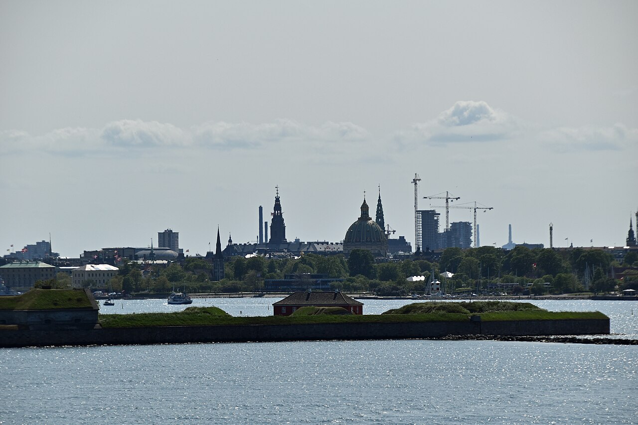 Copenhagen skyline across calm harbour water, with the Marble Church dome, church spires and construction cranes