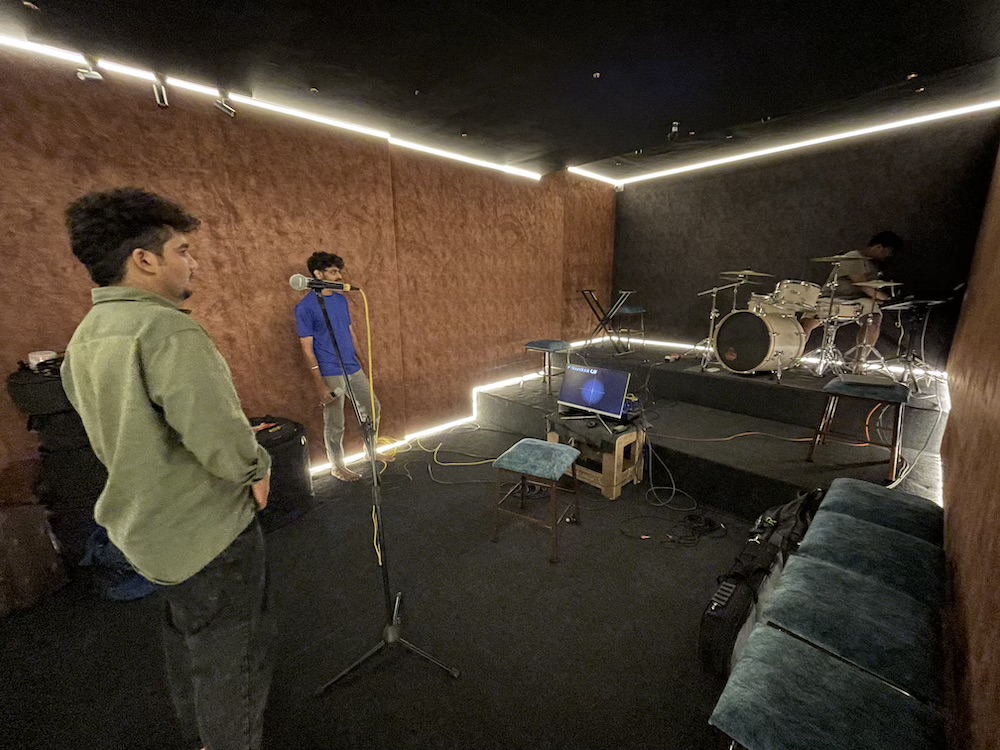 A singer at the mic stand while the drummer plays behind