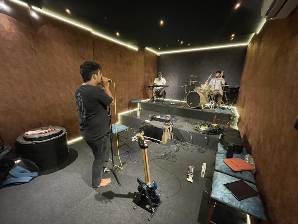 A vocalist running a take with keys and drums on the riser