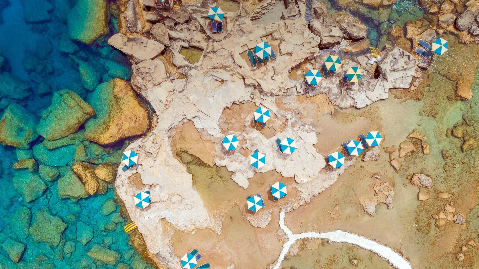 Aerial view of blue and white parasols on the rocky coast of Rhodes, an island in Greece - Amazing Aerial Agency/Offset by Shutterstock)