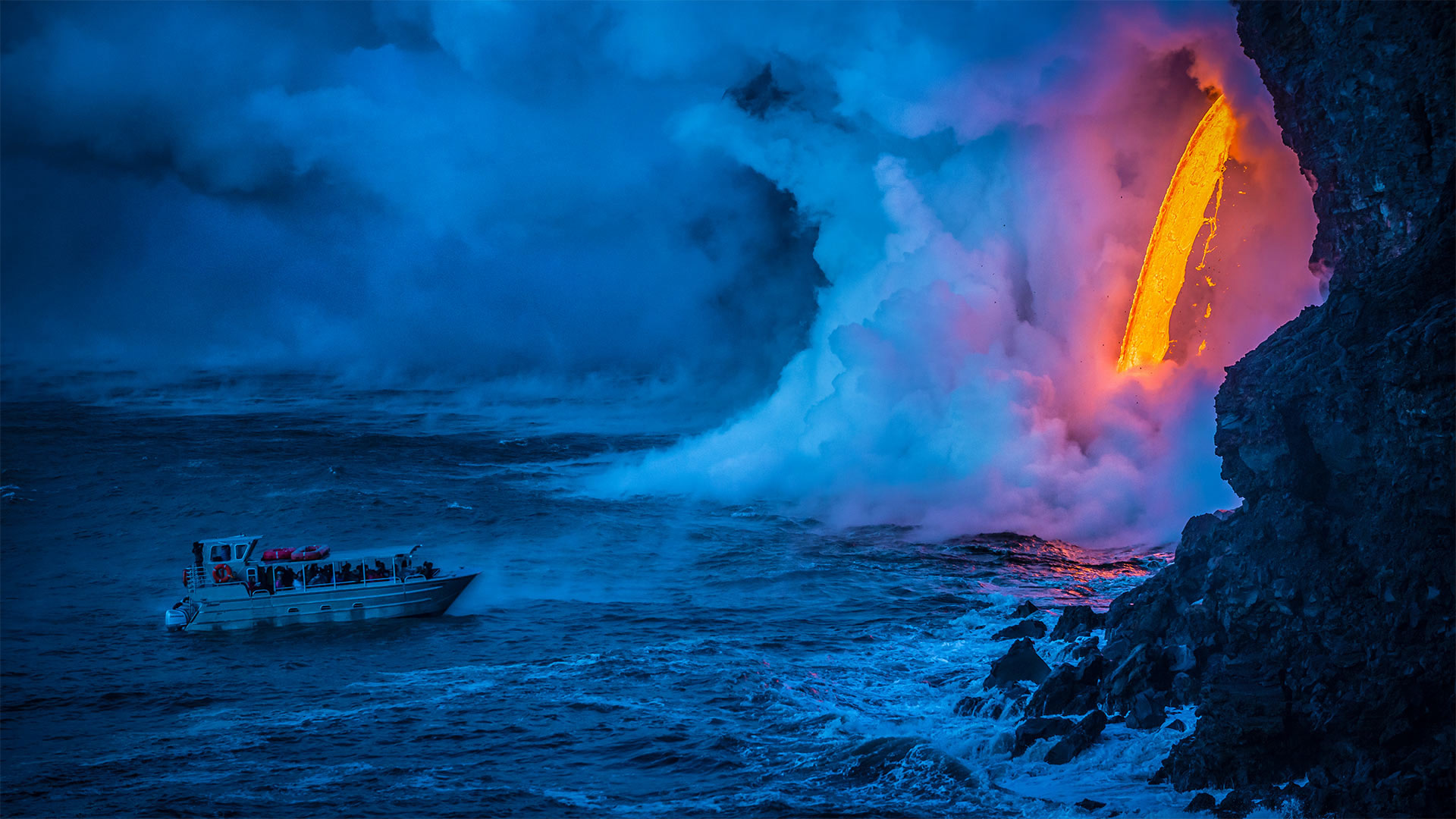 A lava flow hits water as a tour boat passes, Hawaii Volcanoes National Park - Patrick Kelley/Getty Images)