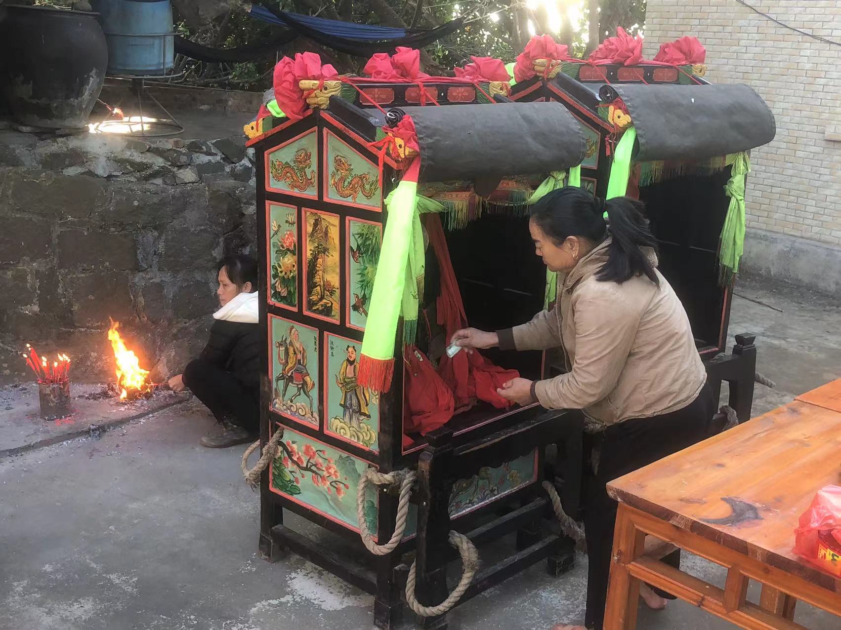 一位村民在给神像递现金，另一位村民在水仙大王的香炉面前烧纸钱