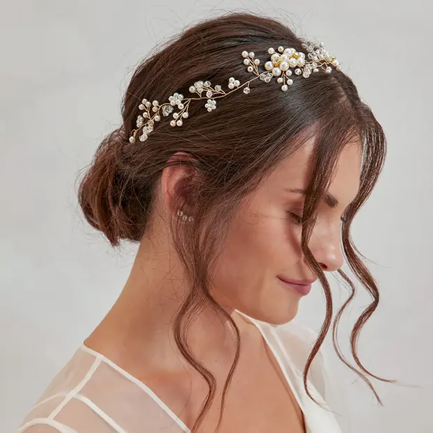 Une femme aux châtain foncé, coiffés en un chignon bas et lâche, avec un accessoire capillaire délicat.