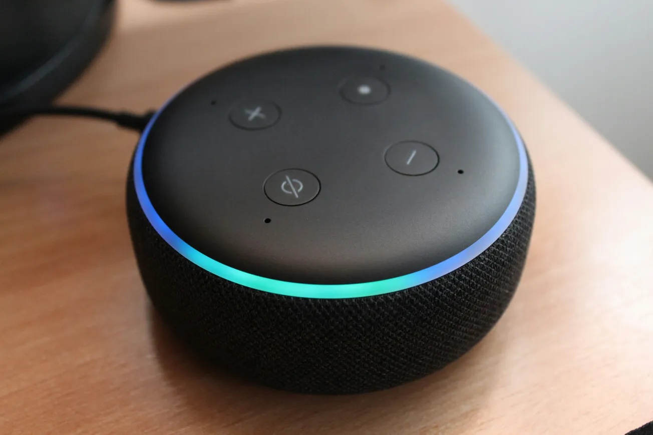 smart speaker on a wooden table with a glowing blue ring. its black surface features four buttons, conveying a tech-savvy and modern feel.